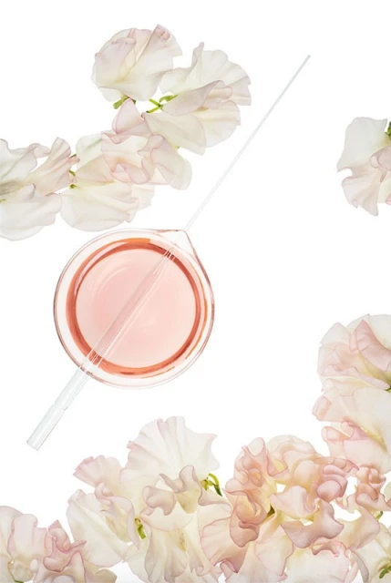 Laboratory beaker filled with pink liquid and a pipette, surrounded by white sweet pea flowers on a white background in a studio shot.