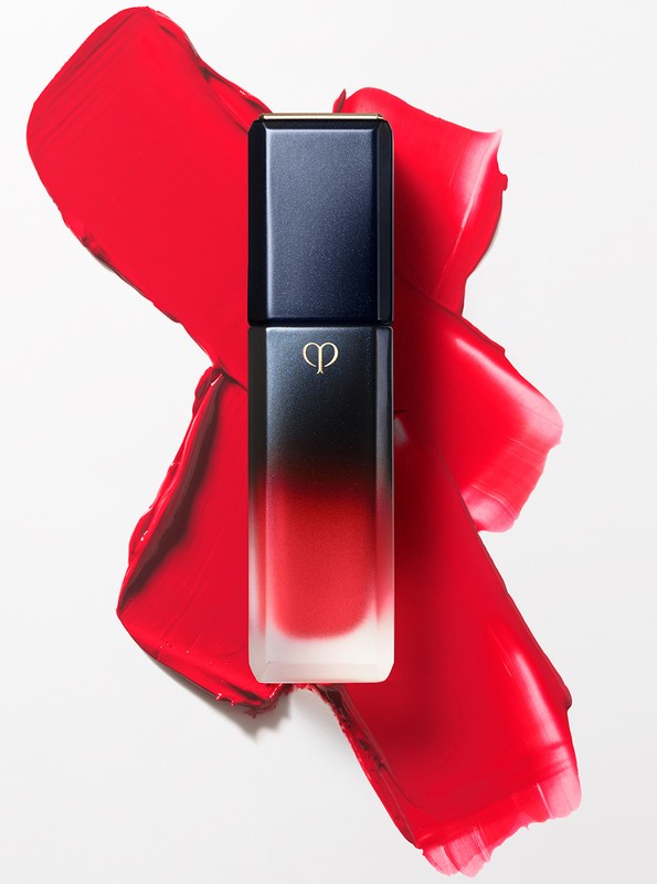 Elegant black and red ombre lipstick in its container surrounded by smeared red lipstick on a bright white surface.
