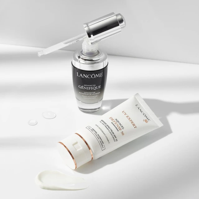 Lancôme skincare product duo featuring Advanced Génifique serum and UV Expert sunscreen, presented on a white surface with soft, diffused lighting.