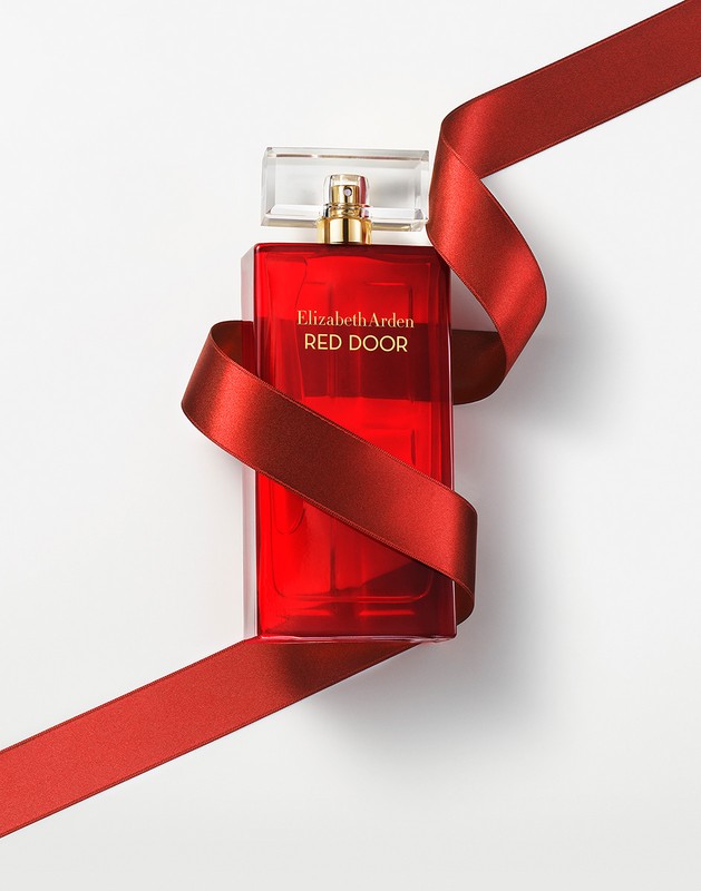 Elegant studio shot: red Elizabeth Arden Red Door perfume bottle with clear cap, wrapped in satin ribbon against a white background.