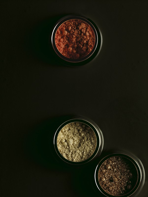 Three metal containers with multi-toned bronzer powder on a dark background, makeup product flat lay for beauty advertising purposes.