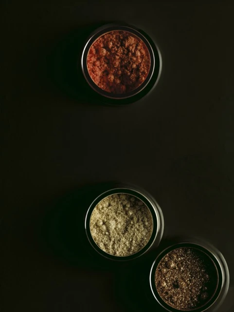 Three metal containers with multi-toned bronzer powder on a dark background, makeup product flat lay for beauty advertising purposes.