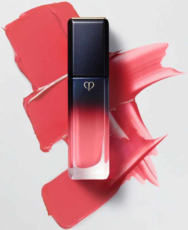 Cosmetic still life: close-up of lip gloss tube with black cap and coral smear on a white surface, beauty product presentation.