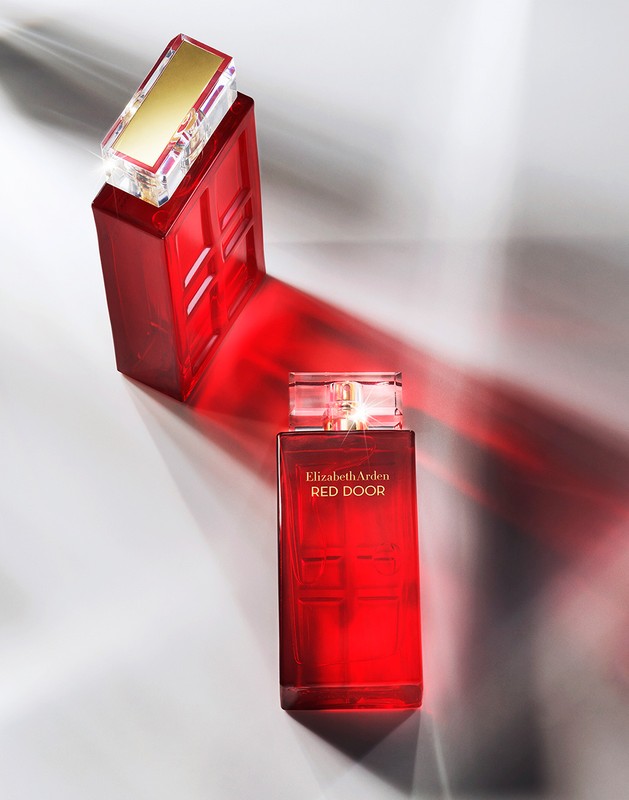 Overhead studio shot of a red Elizabeth Arden Red Door perfume bottle with its cap and reflective light and shadow on a grey surface.