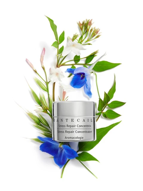 Chantecaille Stress Repair Concentrate+ surrounded by white and blue flowers, and green leaves against a bright white backdrop.