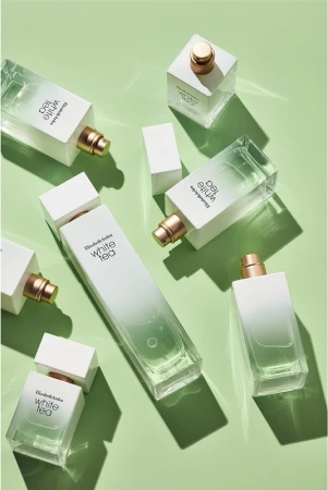 Flat lay of multiple Elizabeth Arden White Tea perfume bottles arranged diagonally on a light green surface with soft shadows.