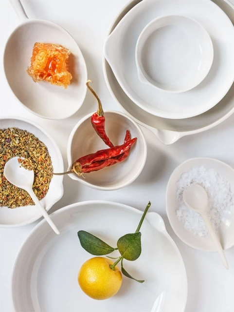 Overhead shot of food ingredients in white ceramic bowls: honey, spices, chili peppers, salt, and a tangerine against a white backdrop.