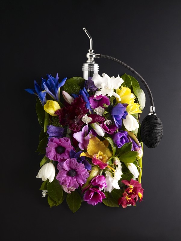 Floral arrangement in the shape of a perfume bottle features bright mix of colors with various blooms and green leaves on black backdrop.