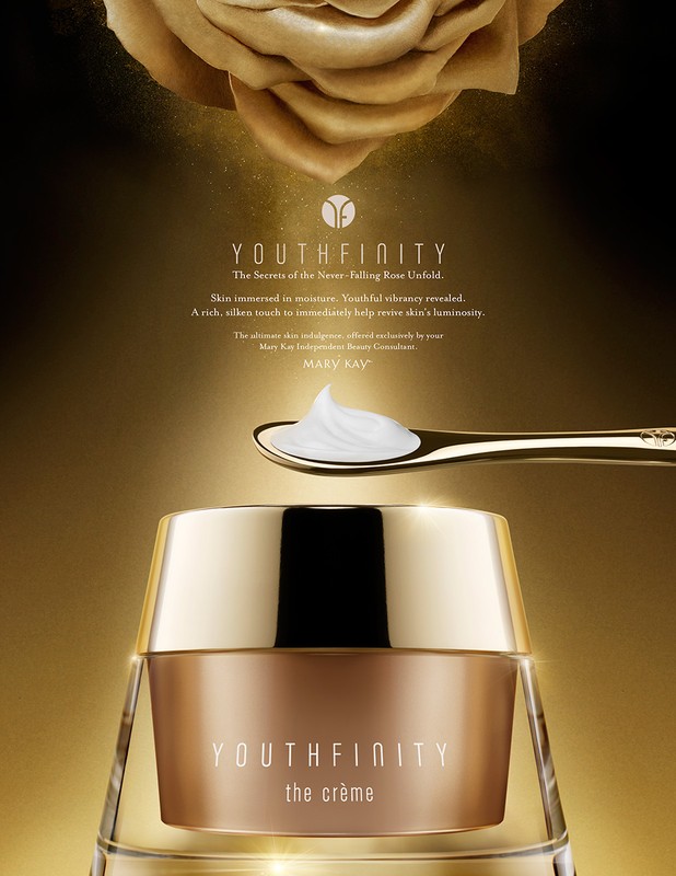 Close-up studio shot of Youthfinity the creme moisturizer in gold packaging, gold spoon with white cream, and gold rose in background.