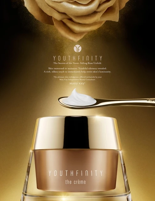 Close-up studio shot of Youthfinity the creme moisturizer in gold packaging, gold spoon with white cream, and gold rose in background.