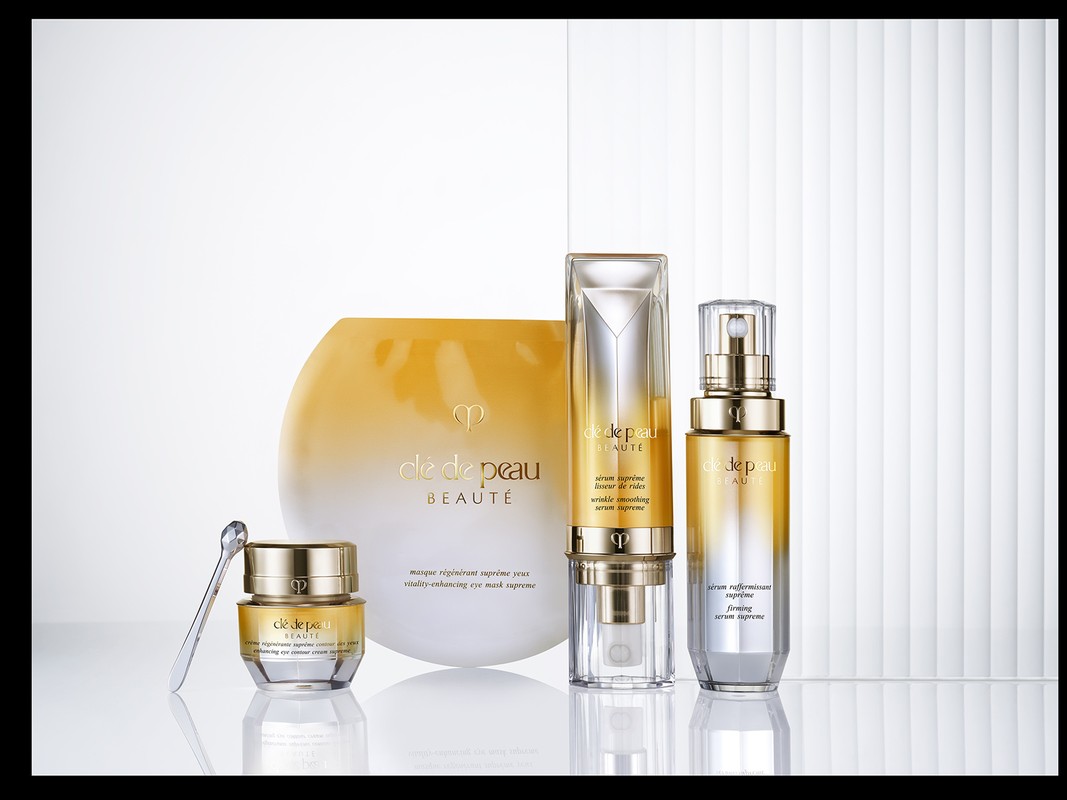 Cle de Peau Beaute skincare bottles and jars with gold ombré gradient arranged on a white reflective surface.