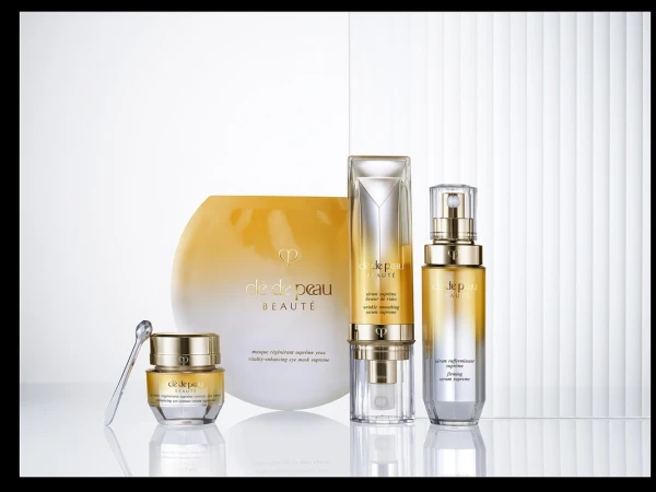 Cle de Peau Beaute skincare bottles and jars with gold ombré gradient arranged on a white reflective surface.