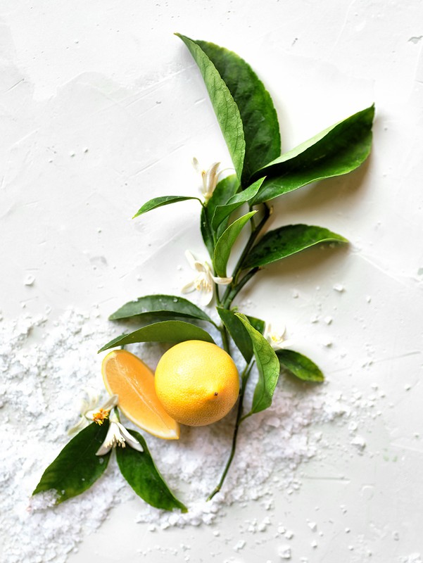 Overhead shot of fresh lemons with leaves and blossoms on a white textured surface, showcasing the vibrant colors and natural arrangement.