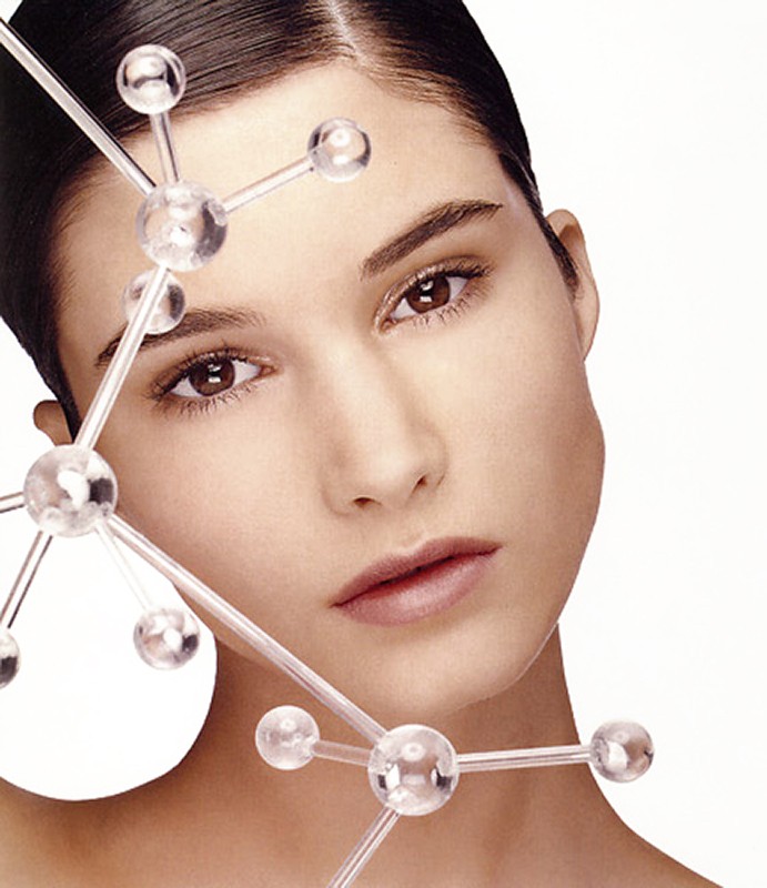 Close-up of woman's face with light skin, brown eyes, neutral expression, and clear molecule model over face on a white background.