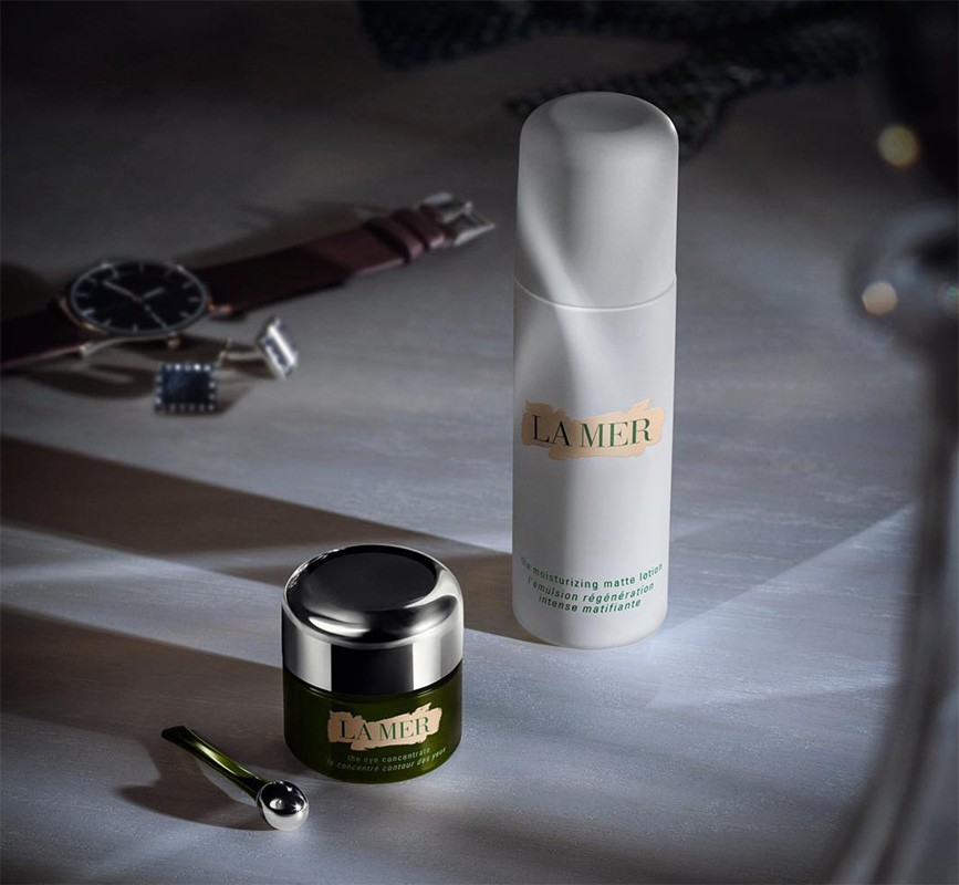 La Mer skincare products on a surface with a watch and cufflinks in the background, conveying a sense of luxury and self-care.
