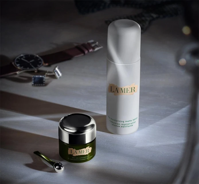 La Mer skincare products on a surface with a watch and cufflinks in the background, conveying a sense of luxury and self-care.