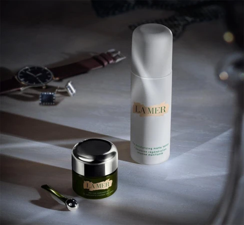La Mer skincare products on a surface with a watch and cufflinks in the background, conveying a sense of luxury and self-care.
