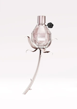 Faceted glass perfume bottle shaped like a grenade resting on a sculpted rose stem against a white background.