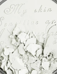Crumbled white pressed powder compact with engraved cursive script styling by prop stylist Beverley Hyde