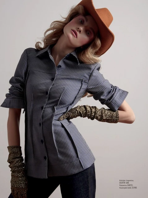 Fashion portrait of a blonde woman in a patterned blue shirt, cowboy hat, and metallic gold gloves, posing against a neutral background.