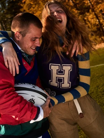 Two people laughing with a rugby ball outdoors, styled by Blair Petty