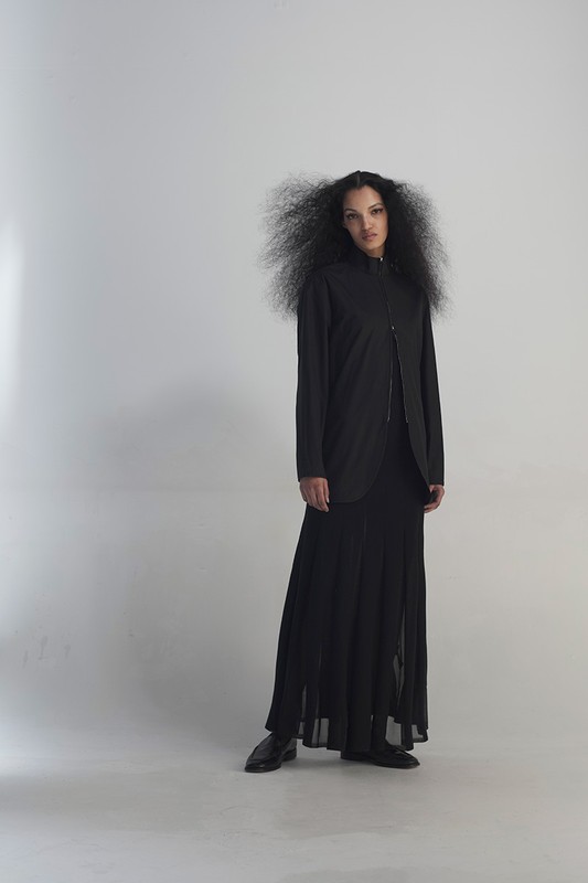 Full-length portrait of a stylish young woman with an afro in a black jacket, dress, and shoes, posing in a bright white studio.