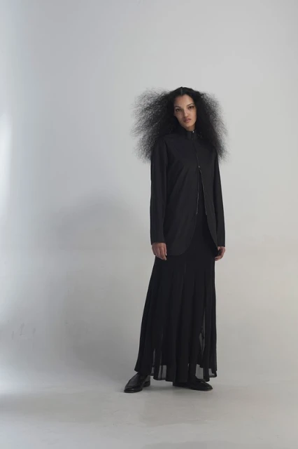 Full-length portrait of a stylish young woman with an afro in a black jacket, dress, and shoes, posing in a bright white studio.