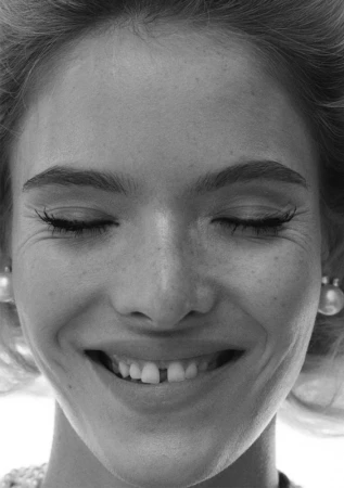 Close-up black and white portrait of a smiling woman with closed eyes and visible pearl earrings by hair stylist Blair Petty.