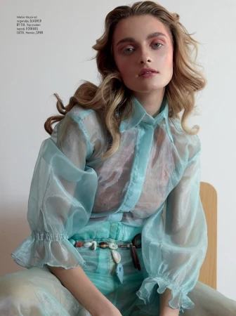 Portrait of a blonde woman wearing a sheer light blue button-down shirt and beaded belt in Los Angeles.