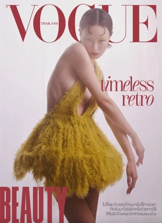 Model in a yellow feathered mini dress with sheer tights posing against a plain background for a magazine cover.