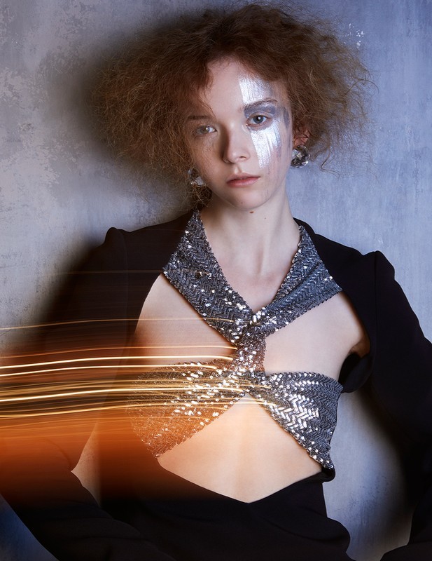 Stylish young woman with silver eyeshadow, silver beaded top, and black blazer in a fashion portrait with light painting effect.