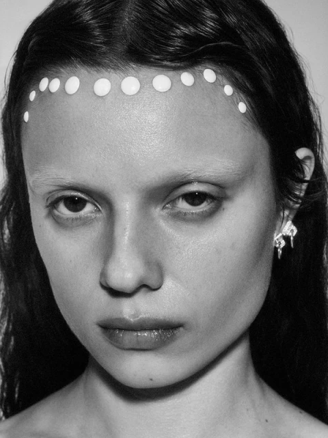 Black and white portrait of a woman with white paint dots on her forehead and artistic earrings. Beauty shot with a white background.