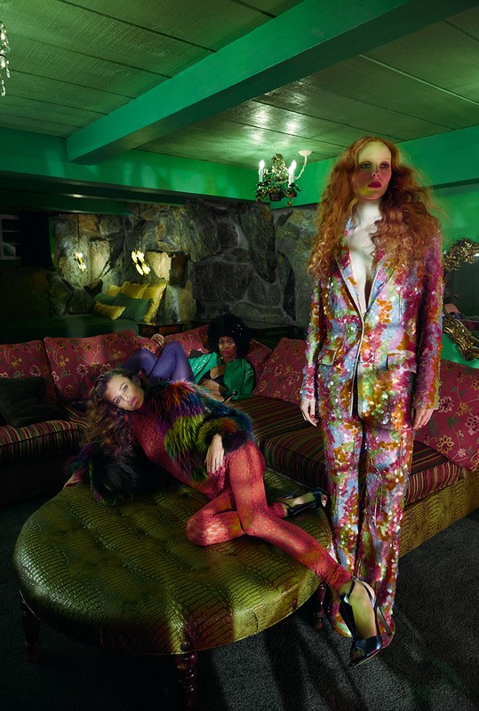 Three diverse fashion models showcase bold patterned outfits in an eccentric indoor setting with green walls and retro decor.