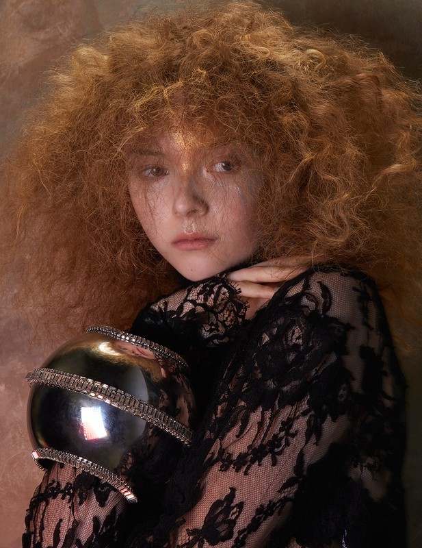 Portrait of a redhead with a black lace top holding a silver orb, creating an artistic, fashion-focused image with warm lighting.