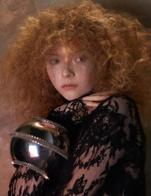 Portrait of a redhead with a black lace top holding a silver orb, creating an artistic, fashion-focused image with warm lighting.