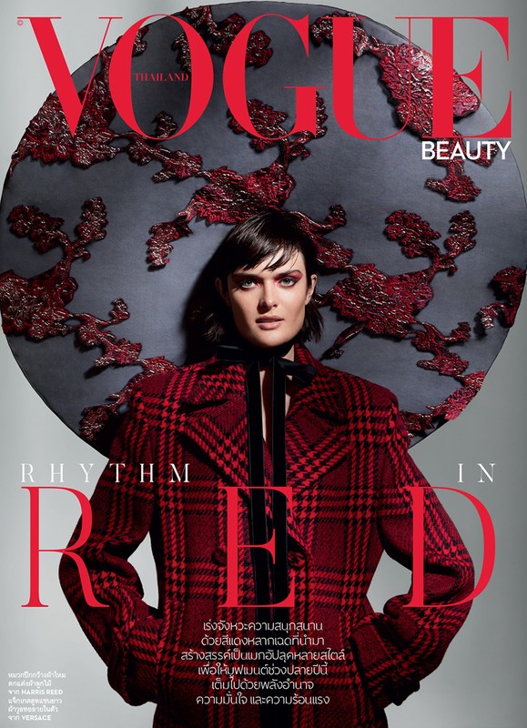 Vogue magazine cover featuring a female model wearing a red plaid jacket and a large, ornate hat in a photo studio setting.