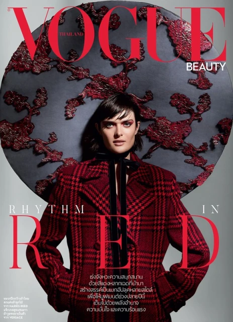 Vogue magazine cover featuring a female model wearing a red plaid jacket and a large, ornate hat in a photo studio setting.