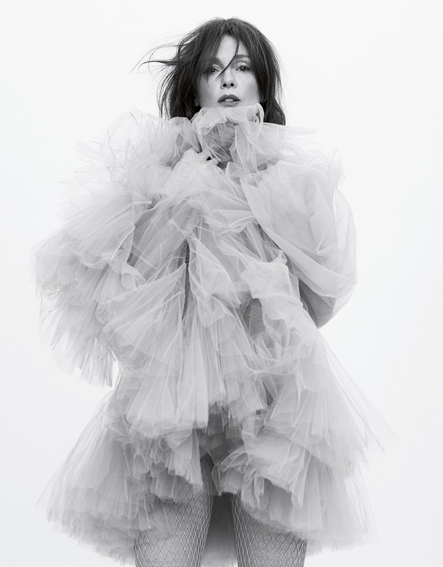 Woman in a voluminous, tiered tulle dress poses in a studio. The black and white portrait captures a light, airy, and elegant aesthetic.
