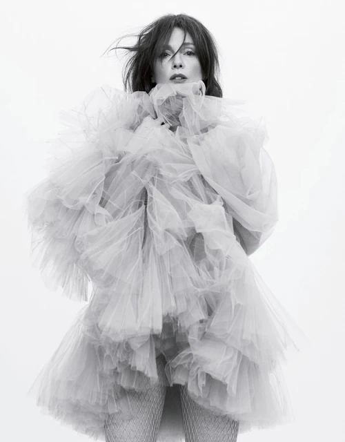 Woman in a voluminous, tiered tulle dress poses in a studio. The black and white portrait captures a light, airy, and elegant aesthetic.