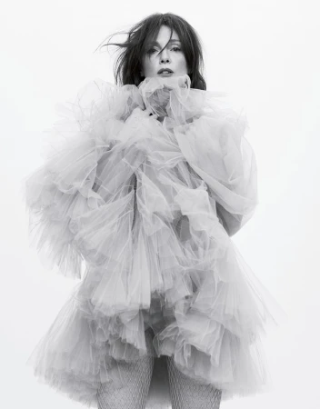 Woman in a voluminous, tiered tulle dress poses in a studio. The black and white portrait captures a light, airy, and elegant aesthetic.