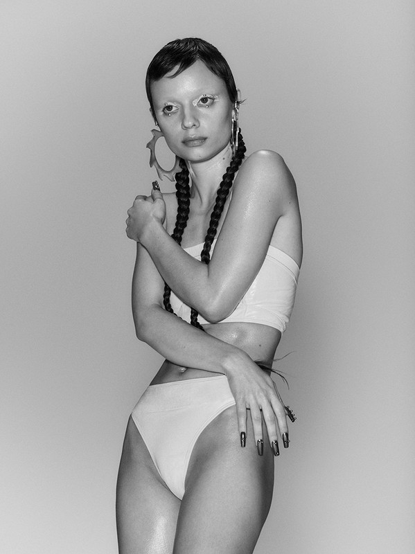 Striking studio shot of a model with unique braids and striking geometric earrings, posing in a contemporary top and high-cut bottoms.