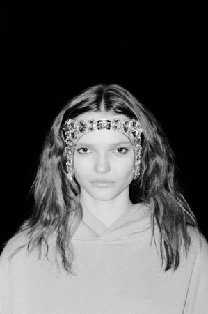 Model wearing a crystal jeweled headpiece and hoodie against a black background