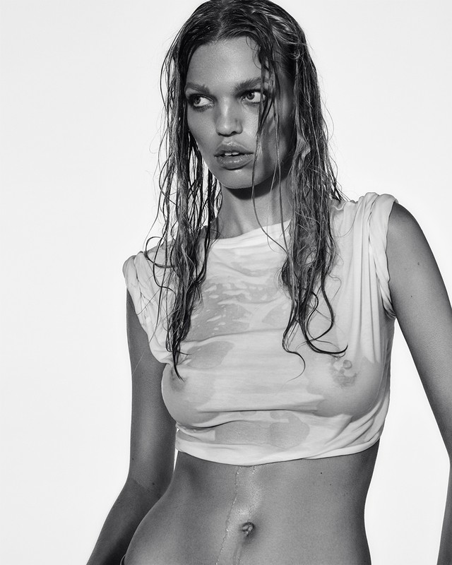 Black and white portrait of an adult woman with wet hair and a wet t-shirt, against a bright, plain background in a studio setting.