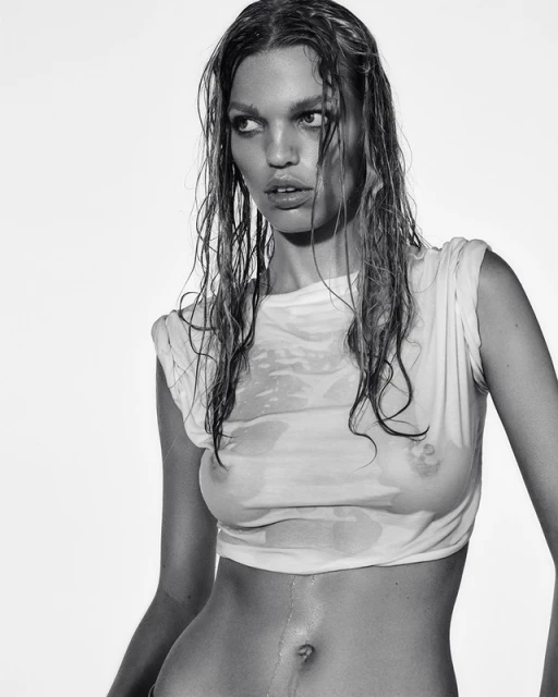 Black and white portrait of an adult woman with wet hair and a wet t-shirt, against a bright, plain background in a studio setting.