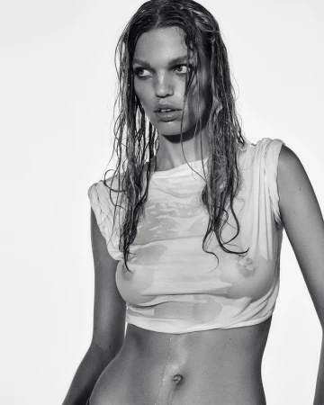 Black and white portrait of an adult woman with wet hair and a wet t-shirt, against a bright, plain background in a studio setting.