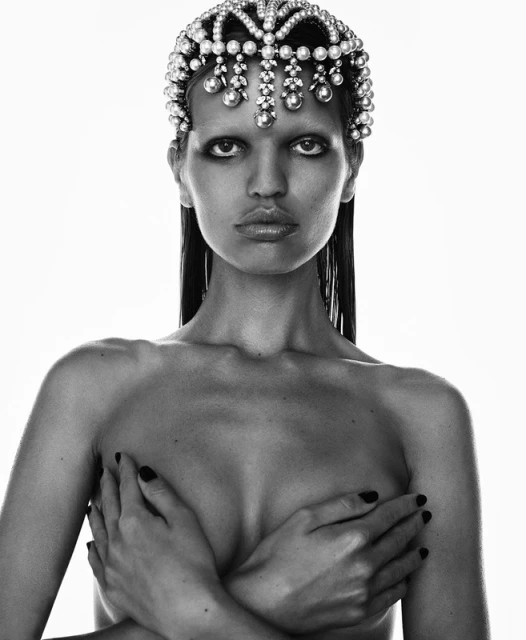 Striking black and white fashion portrait of a model wearing an ornate jeweled headpiece, covering her chest with her hands in a photo studio.