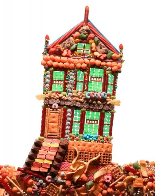 Quirky, colorful food house artfully constructed from cookies, crackers, candies, and other sweets on a white background.
