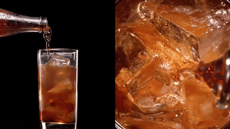 Beverage being poured from a clear bottle into a clear glass filled with ice cubes, on a dark background, drink photography.