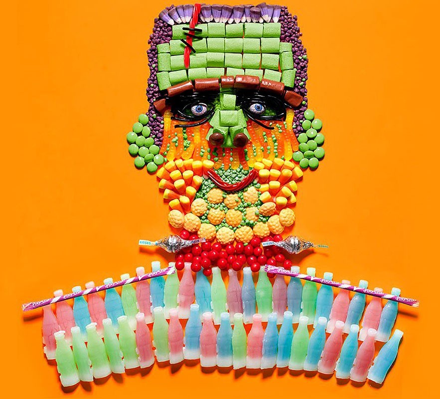 Frankenstein's monster face is constructed from colorful candies, gum, and soda bottles arranged on an orange backdrop.