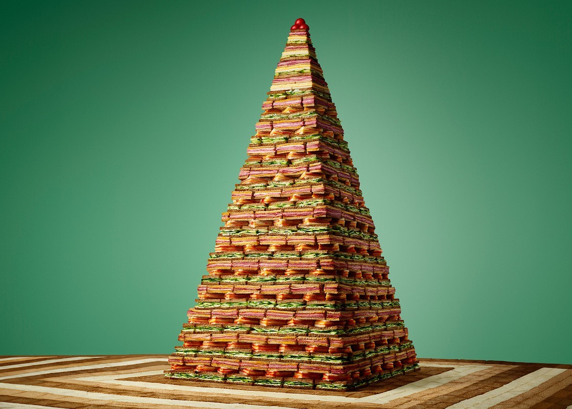 Tower of sandwiches stacked in a triangular shape against a green backdrop with a striped brown rug underneath for a food concept.